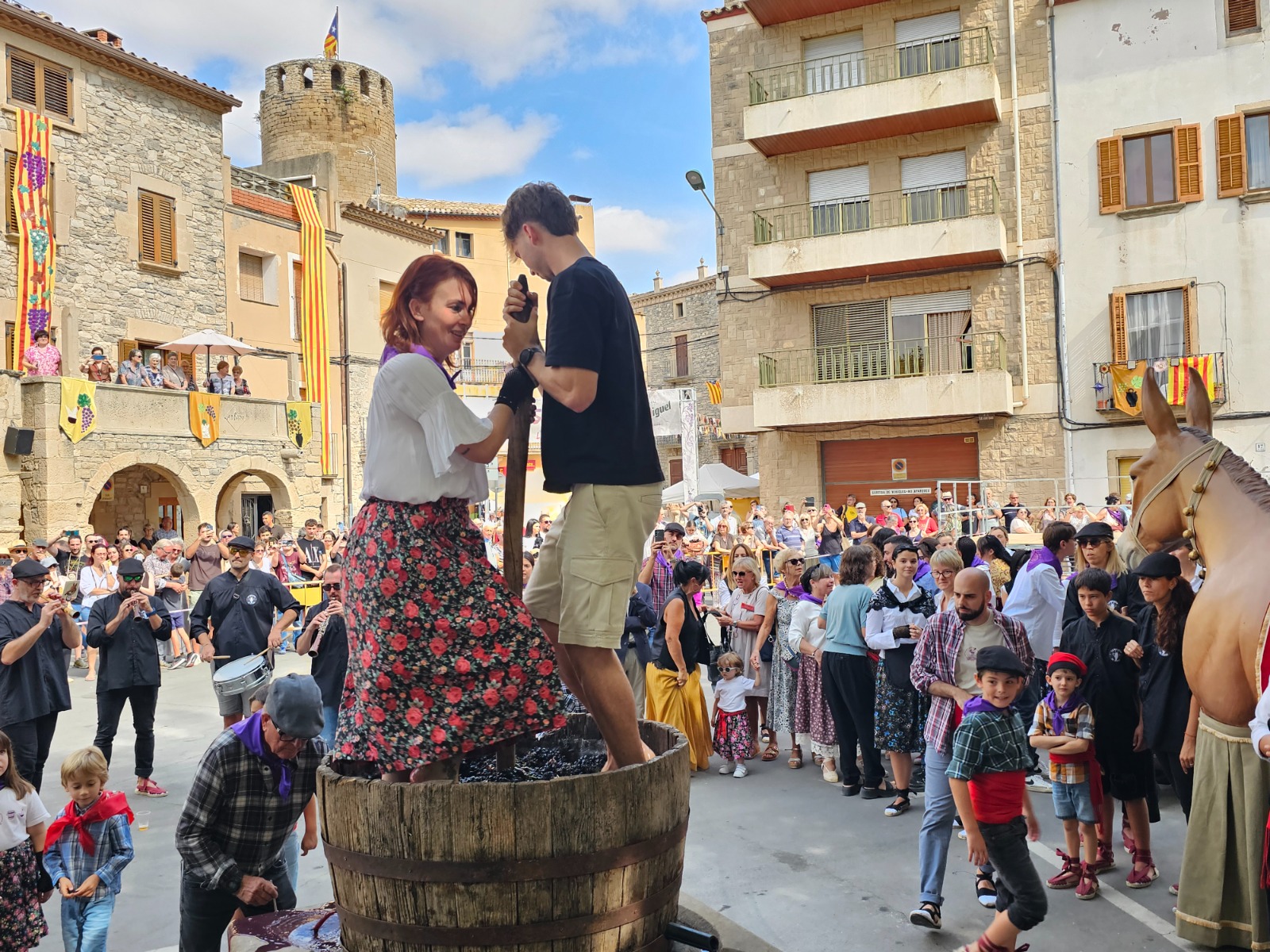 Parella piant raïm en una tina de fusta a la plaça de Verdú, amb la torre del castell al fons, Bacus 2026